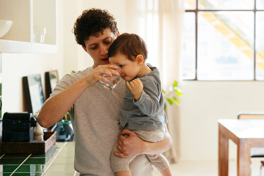 Father with toddler son drinking a glass of water at modern home