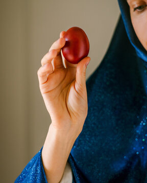 Female hand covered with blue velvet cloth holds a red Easter egg