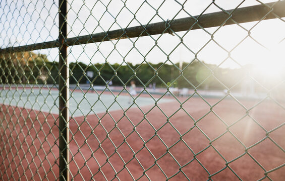 Tennis court view through a chain-link fence at sunset