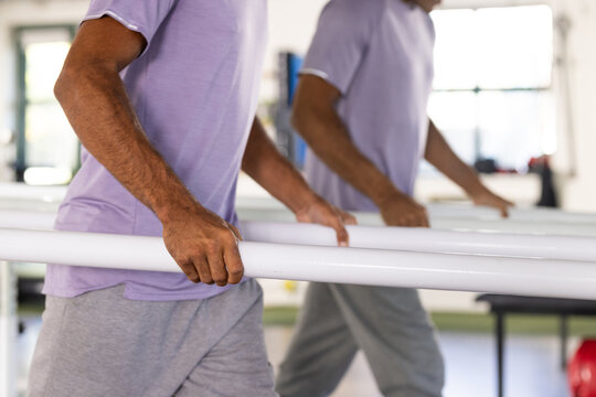 A biracial male patient in purple shirt holds parallel bars at a rehabilitation center