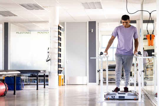 A biracial male patient walking at gym rehabilitation center between parallel bars, copy space