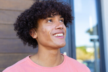 A biracial young male wearing pink shirt, smiling outdoors
