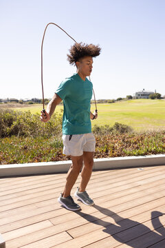 A biracial young male jumping rope outdoors, wearing sporty attire