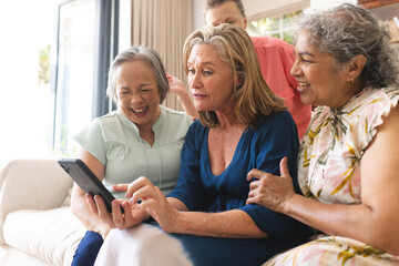Diverse senior female friends laughing at home, looking at tablet - Powered by Adobe