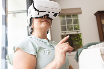 A senior Asian woman wearing virtual reality headset at home, pointing