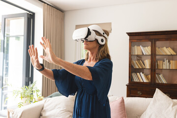 A senior Caucasian female wearing VR headset at home, standing in a living room