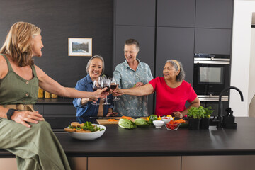 Diverse senior female friends enjoying drinks at home in kitchen