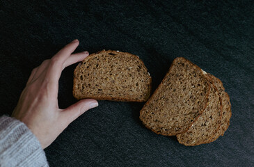 A woman's hand holds a piece of bread with sunflower seeds.