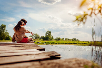 Young couple in love fishing sitting on bridge across lake holding rod on spring day. Outdoor...
