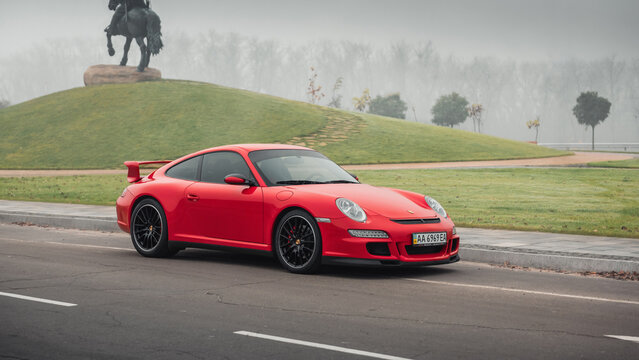 Red Porsche 911 on a foggy morning. Three quarter view of Porsche 997 sportscar in front of horseback monument on a hill. Kyiv, Ukraine - November 10 2018.