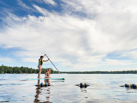 Woman teaching young girl Sup paddleboard calm lake in New Hampshire - Powered by Adobe