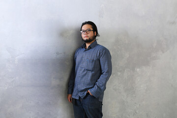 Obraz premium portrait of a cool man standing with his hands in his jeans pockets leaning against the wall background