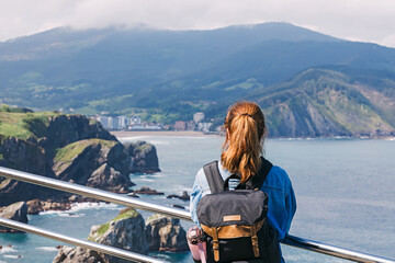 Naklejka premium Woman tourist with a backpack looking on the scenic landscape at San Sebastian, Spain