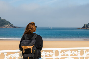 View from the back of the woman tourist with a backpack looking on the beach of San Sebastian, Spain