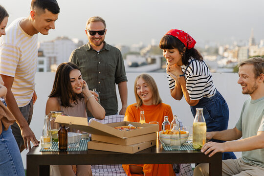 Happy friends eating pizza during rooftop party