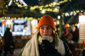 Young woman on Christmas market with blurred lights on background
