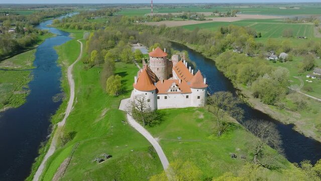 Aerial establishing view of Bauska Medieval Castle and ruins, Musa and Memele rivers next to the castle, sunny spring day, wide drone shot moving forward, camera tilt down