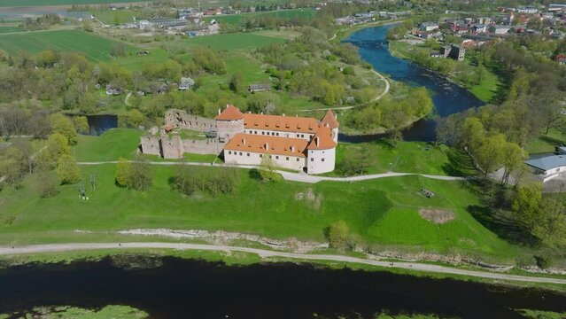 Aerial establishing view of Bauska Medieval Castle and ruins, Musa and Memele rivers next to the castle, sunny spring day, distant orbiting drone shot