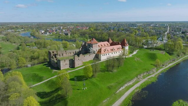 Aerial establishing view of Bauska Medieval Castle and ruins, Musa and Memele rivers next to the castle, sunny spring day, wide drone shot moving forward, tilt down