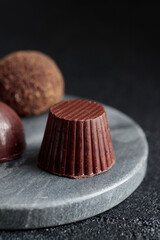 Delicious gourmet chocolate handmade truffles from confectionery, homemade dark chocolate candies on marble plate and black background