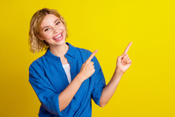 Portrait of pretty young lady direct fingers empty space wear blue shirt isolated on yellow color...