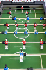 Classic Foosball Table Game With Players in Red and Blue Jerseys During Daytime Indoor Match. Close-up view of foosball table featuring red and blue jersey players positioned for daytime indoor game.