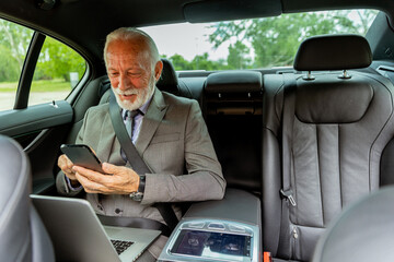 Elderly businessman checking his smartphone while traveling in a luxury sedan