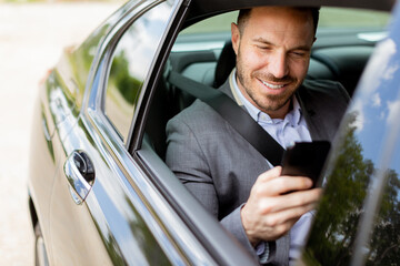 Business executive checking smartphone while riding in luxury sedan on a sunny day