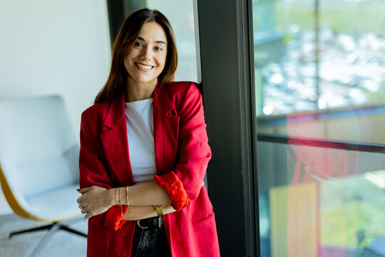 Confident young professional in red blazer smiling at modern office environment
