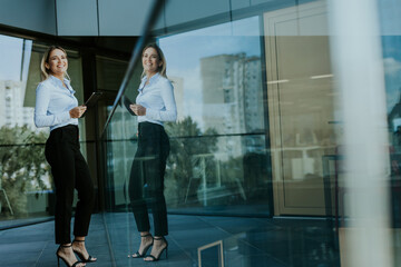 Confident businesswoman holding digital tablet while standing outside modern office building at noon
