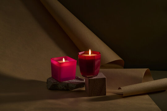 Scented candle in a red glass jar on wood geometric podium. Home decor