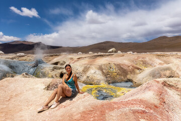 A woman sits on a hill in the background Sol de Mañana geysers in Bolivia