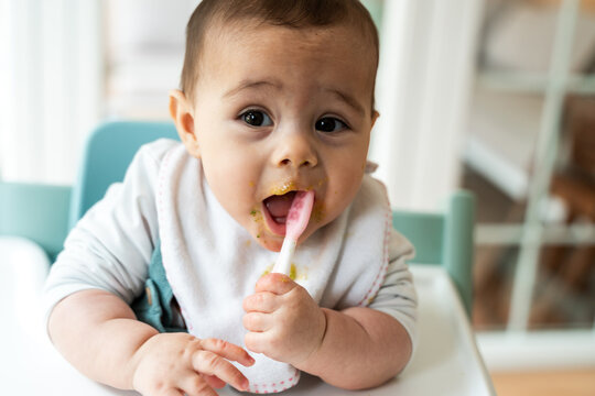 Messy baby enjoying first solids in high chair