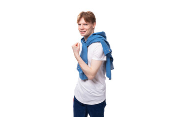 young well-groomed cute caucasian male student with golden red hair with a tattoo on his arms is dressed in a white t-shirt