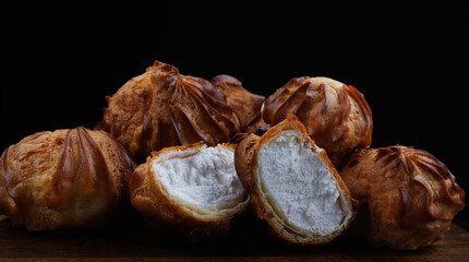 Profiteroles with white custard on a wooden board. Mini eclairs with white cream.