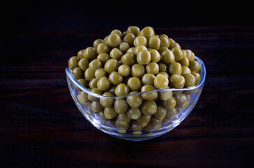 Canned green peas in a glass cup stand on a dark wooden surface.