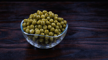 Canned green peas in a glass cup stand on a dark wooden surface.