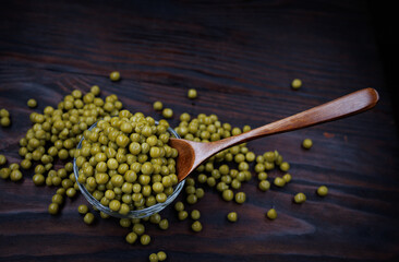Wooden spoon in a glass cup with canned green peas.