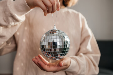 Close-up of the hands of a girl holding a disco ball against the background of a decorated...