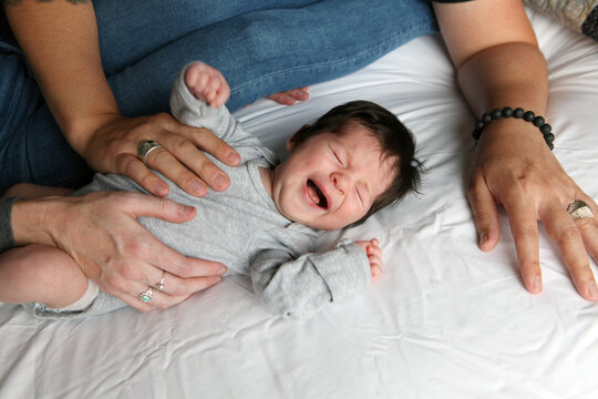 Crying Dark Haired Baby Laying on Bed