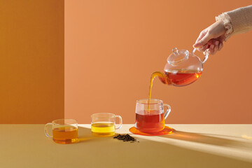 Pouring black tea into glass cup on beige  table