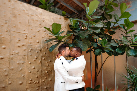 PDA gay grooms romantically kissing in front of quirky gold wall