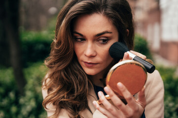 Young woman touching up makeup with brush outside