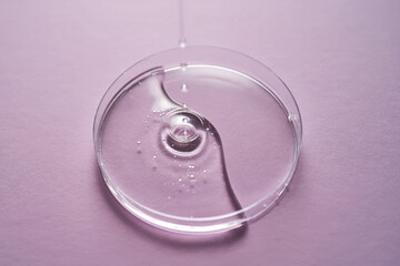 Serum or cosmetic oil flows into a transparent bowl on a purple background.