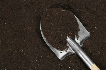 Metal shovel on fertile soil, top view and space for text. Gardening tool