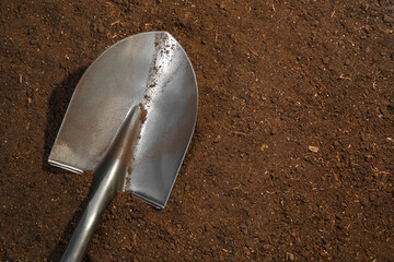 Metal shovel on fertile soil, top view and space for text. Gardening tool