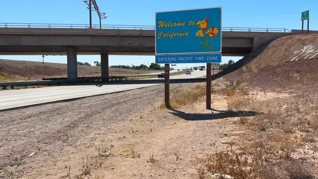 Welcome to California. State border sign along highway. Tilt up reveal from sand in desert to bright blue sky.