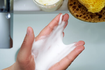 Foam cleanser in female hands over the sink.