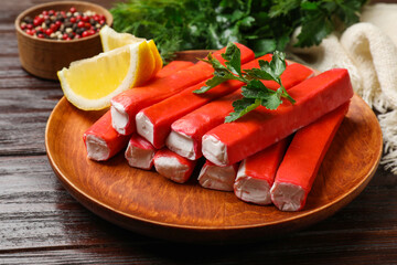 Tasty crab sticks, parsley and lemon wedges on wooden table, closeup