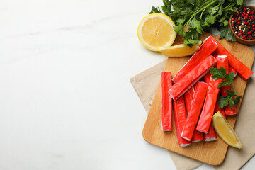 Tasty crab sticks, parsley, pieces of lemon and spices on white table, flat lay. Space for text